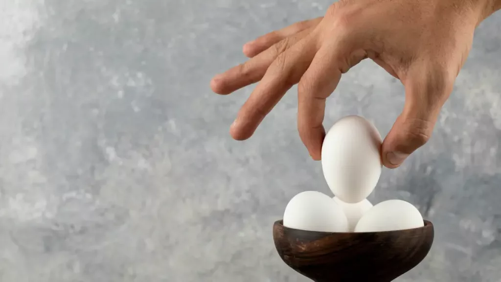 male-hand-taking-raw-egg-from-wooden-bowl