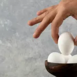 male-hand-taking-raw-egg-from-wooden-bowl