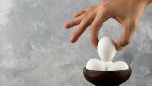 male-hand-taking-raw-egg-from-wooden-bowl