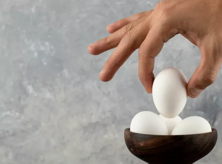 male-hand-taking-raw-egg-from-wooden-bowl